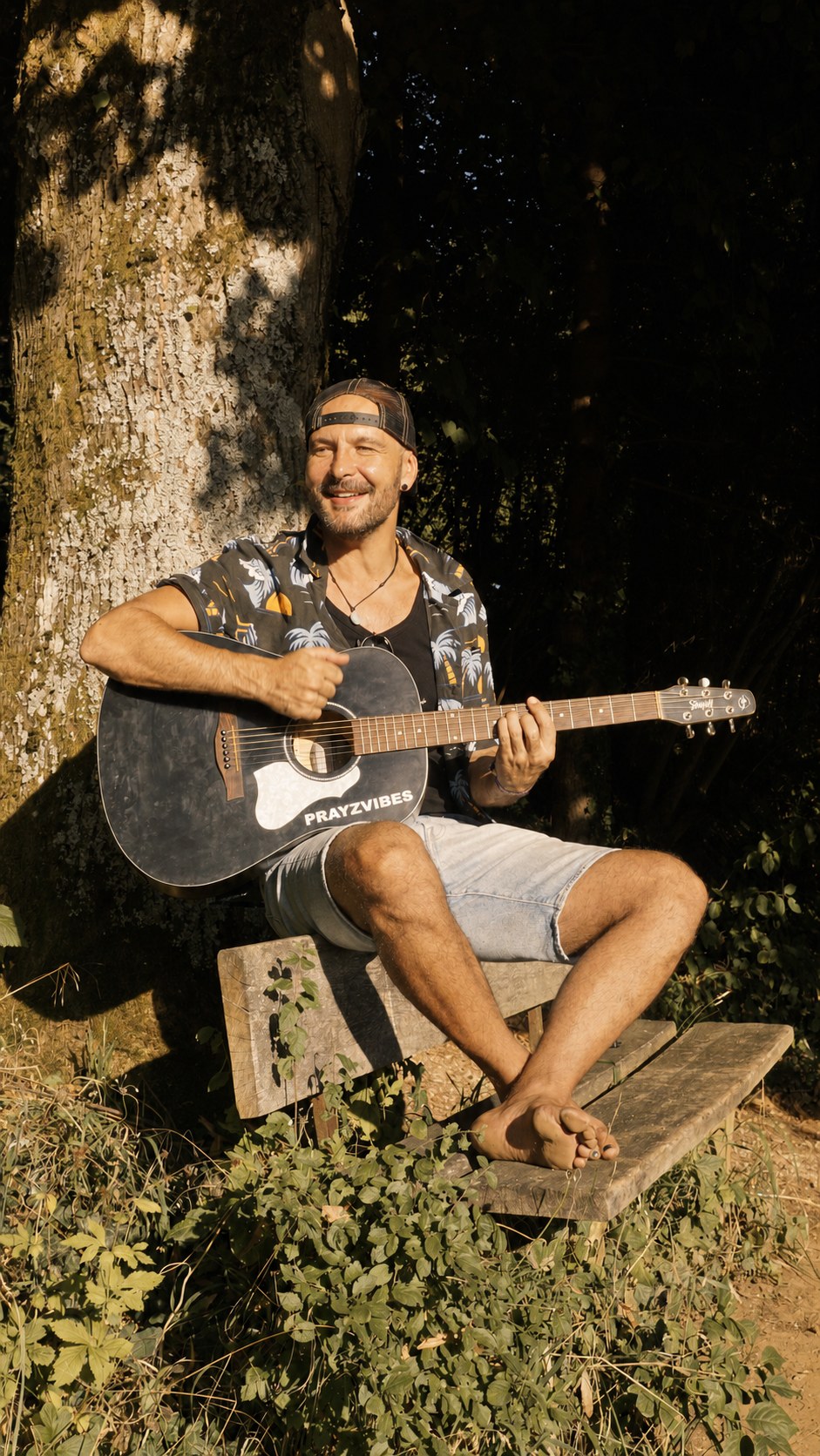 PRAYZ barefoot with his guitar by a tree — original photograph