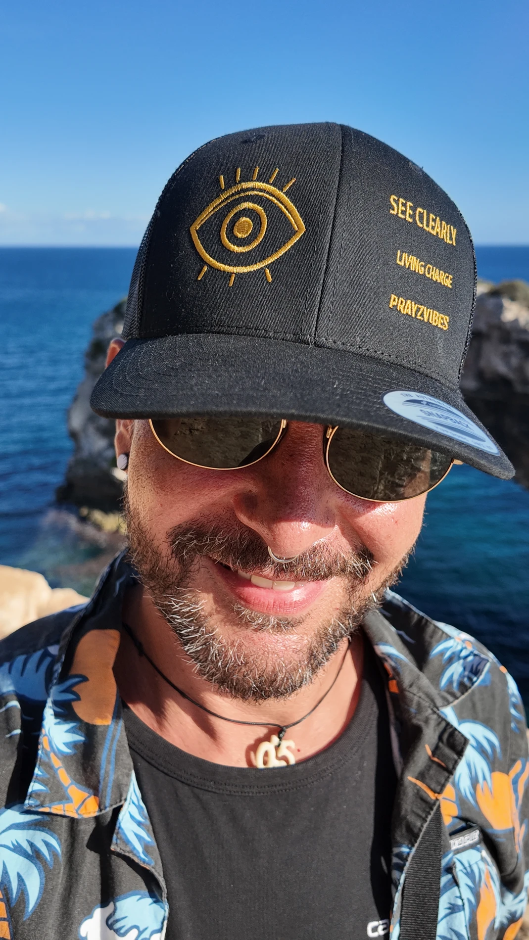 Detail of the actual cap: gold eye embroidery and the words SEE CLEARLY, LIVING CHARGE and PRAYZVIBES
