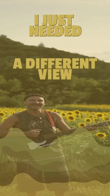 Still from the Mountain Day reel: PRAYZ smiling with a black acoustic guitar in a sunflower field